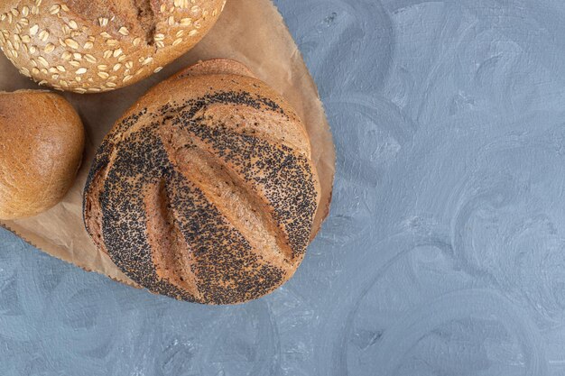 Different bread types bundled on a wooden board on marble table.