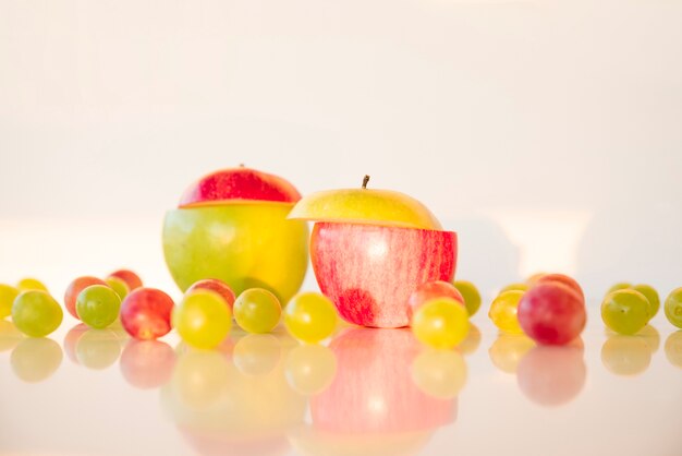 Different colors sliced apple with red and green grapes on reflective desk