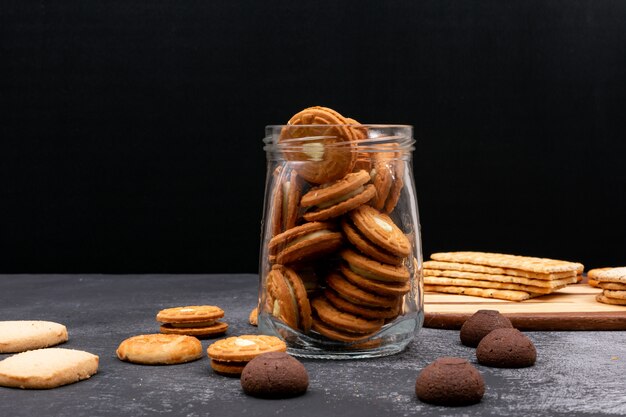 Different cookies in glass jar on dark surface