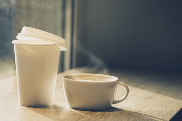 Different cups of coffee - ceramic mug and paper cup to go on wooden table in cafe