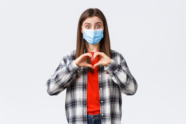 Different emotions, covid-19 pandemic, coronavirus self-quarantine and social distancing concept. Excited young woman in medical mask making confession, show heart sign like someone, express sympathy.