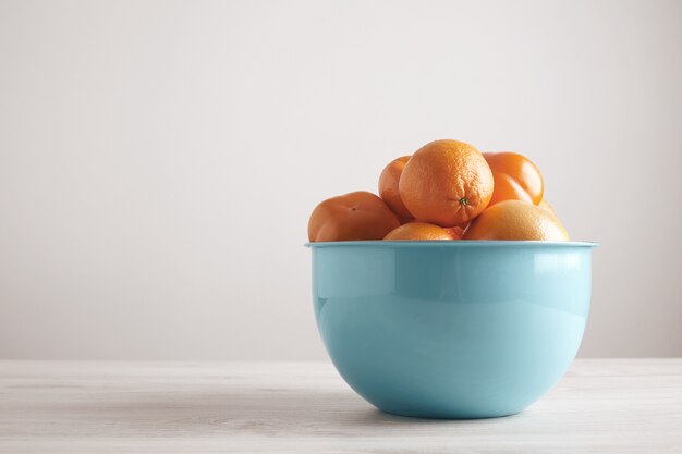 側面から白い木製のテーブルの空白の壁の前に大きな金属製の青いボウルにさまざまな果物と柑橘類