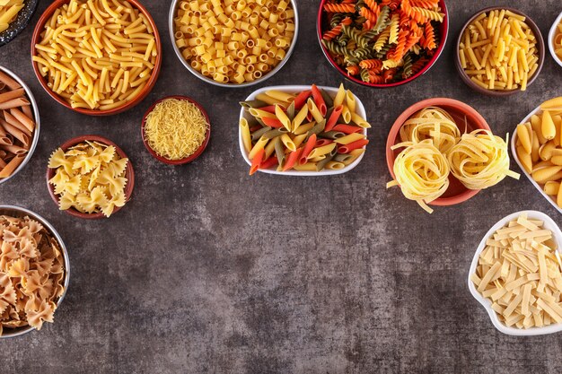 different kids of pasta in plates top view with copy space on gray surface