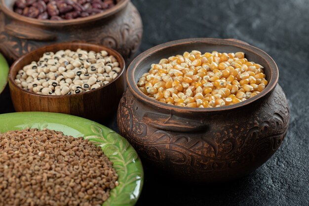 Different kinds of bean seeds, lentil, peas in dishes on black .