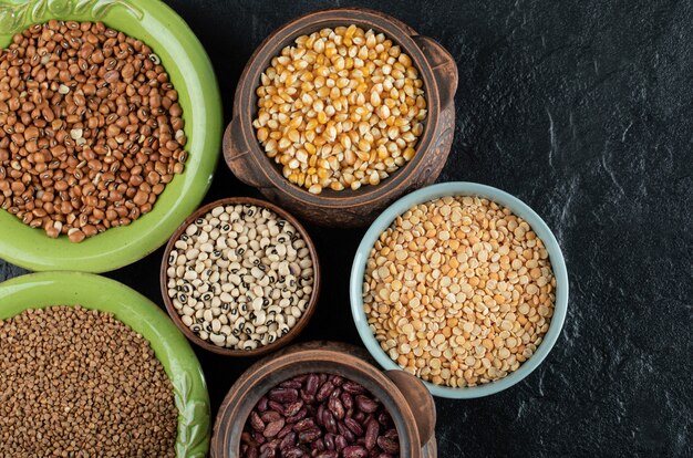 Different kinds of bean seeds, lentil, peas in dishes on black .