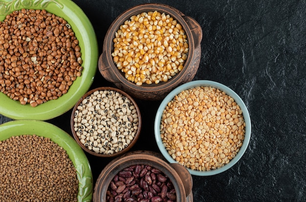 Different kinds of bean seeds, lentil, peas in dishes on black .