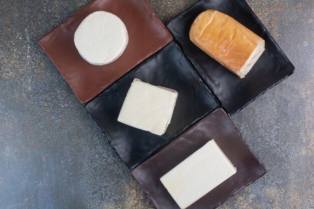 Different kinds of cheese on dark plates.