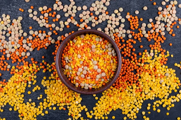 Different lentils in a brown bowl top view on a black stone table