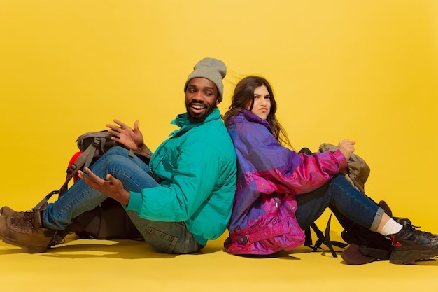 Different look of situation. Portrait of a cheerful young tourist couple with bags isolated on yellow studio background.