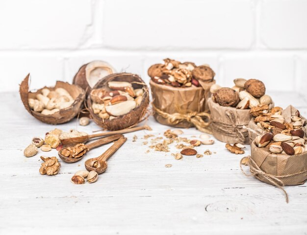 different nuts in plates and wooden spoons closeup on white wooden background ,concept of healthy protein power