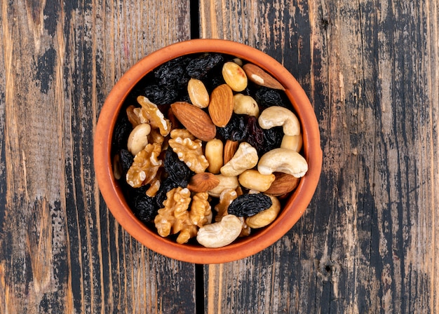 Different nuts and raisins in a brown bowl on a wooden texture table