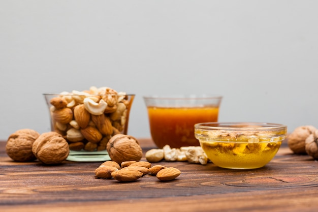 Different nuts with honey in bowls on table