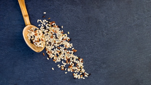 Different rice grains in wooden spoon on table