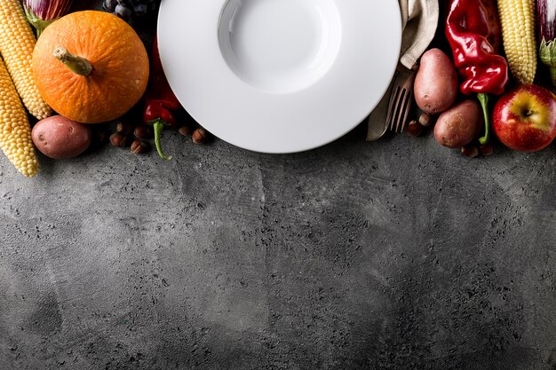 Different seasonal autumn vegetables and fruits with empty plate on grey background