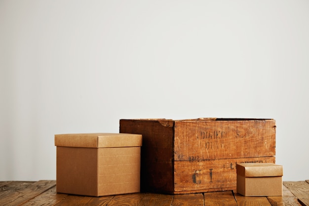 Different sized blank beige corrugated cardboard boxes with covers next to a vintage wine crate isolated on white