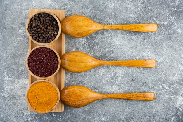 Different spices with wooden spoons on a gray table.
