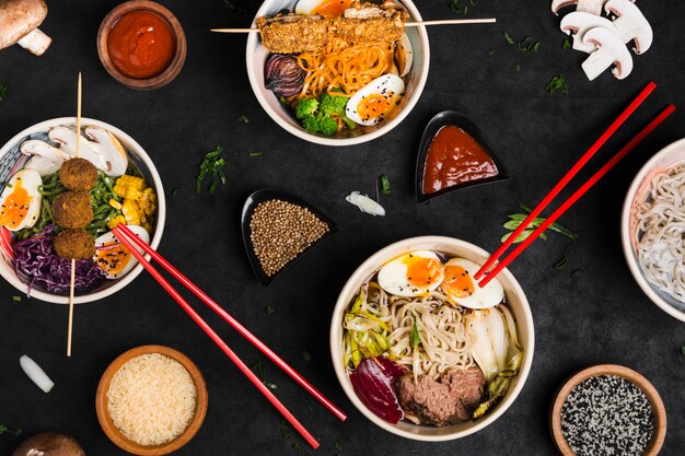 Different type of asian style ramen noodles with sauce; rice and sesame seeds on black textured backdrop