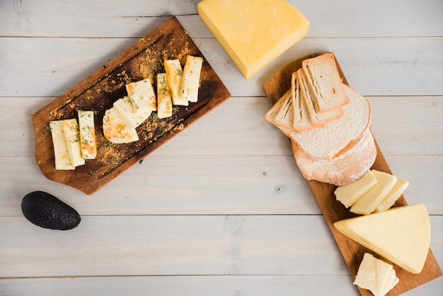 Different type of cheese slices arranged on wooden tray with avocado over the desk