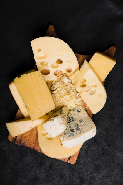 Different type of cheese on wooden board over the black background