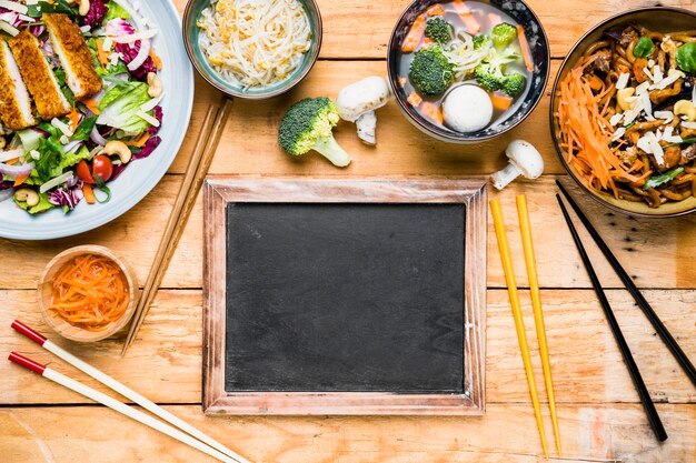 木製の机の上のタイのおいしい食べ物とスレートの近くの箸の種類