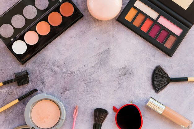 Different type of colorful makeup palette with lipstick; compact powder; brush; mascara; sunglasses; on concrete background