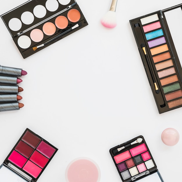 Different type of colorful makeup palette with lipstick; sponge and compact powder on white backdrop