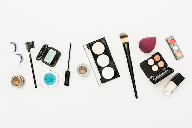 Free photo different type of cosmetics palette with eyeshadow; nail polish bottle and brushes on white backdrop
