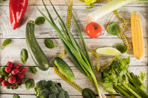 Different type of fresh vegetables with measuring tape on wooden desk