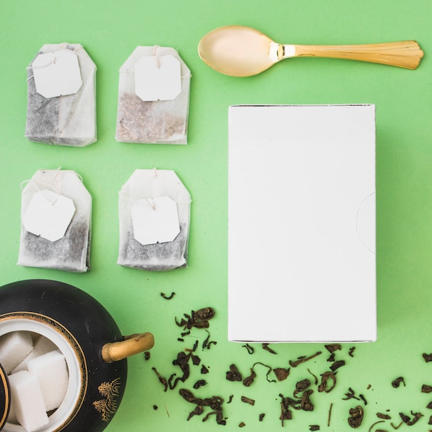 Different type of herbal tea bags, sugar cubes, spoon and white box on colored background