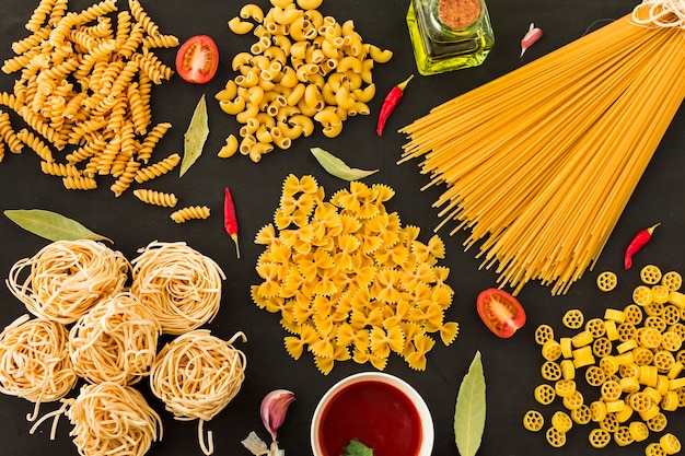 Different type of raw pasta with ingredients on black background