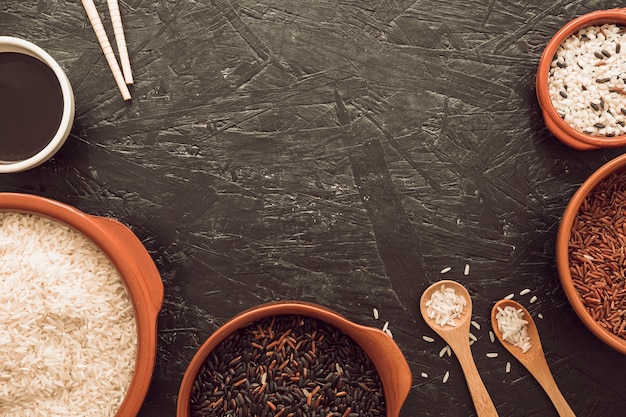 Разный тип чашки с зерном из риса с соевым соусом; палочки для еды и деревянная ложка
