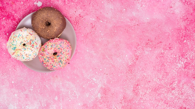 Different type of three donuts on stainless steel against pink background