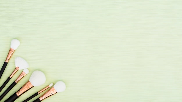 Different type of white makeup brushes on the corner of the green mint background