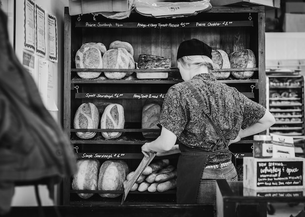 Different types of bread on bakery shelves, baker woman