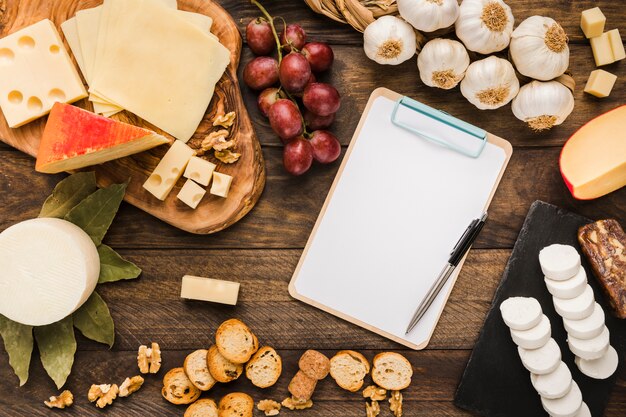 Different types of cheese and blank clipboard on table