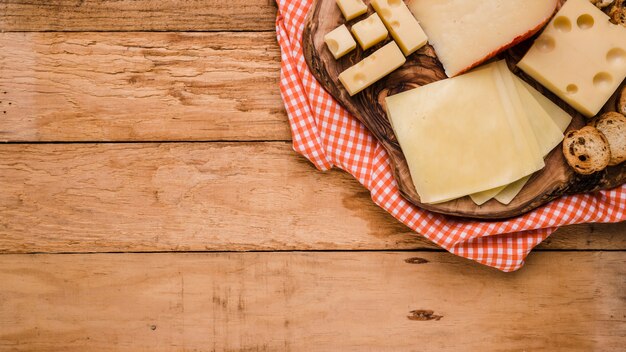 Different types of cheeses on wooden coaster with table cloth over bench