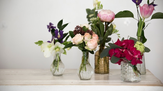 Different types of flowers in the glass vase on desk against white wall
