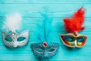 Free photo different types of masquerade carnival mask with feather on blue wooden table