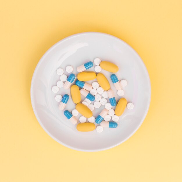 Different types of pills on white plate over yellow background