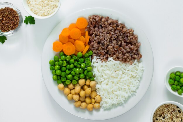 Different types of porridge with vegetables on plate with rice bowls on table