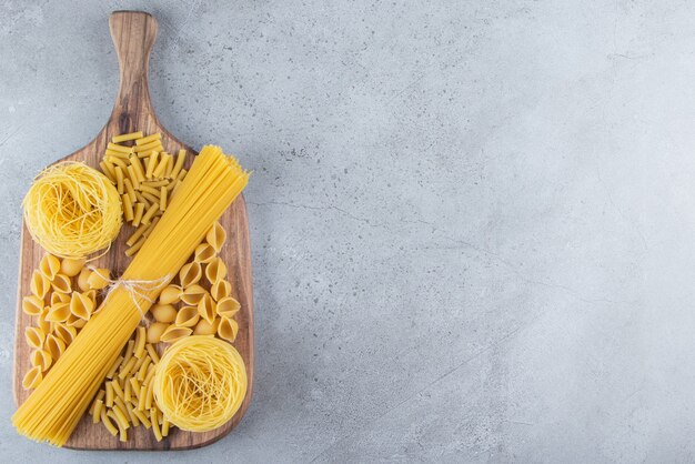 Different types of raw dry pasta on a stone background. 