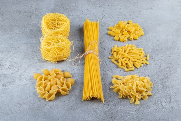 Different types of raw dry pasta on a stone surface.