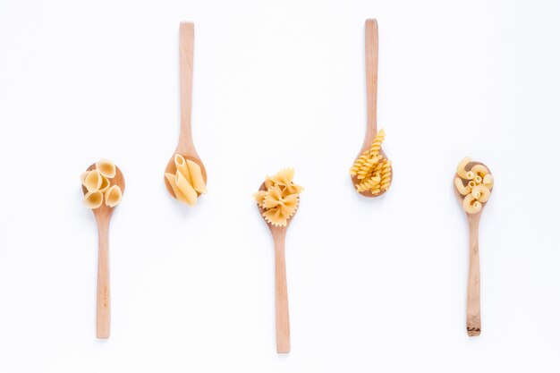 Different types of raw italian pasta on wooden spoon over white surface