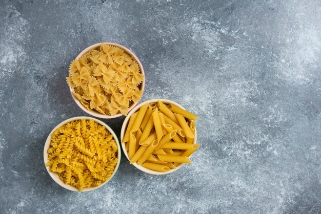 Different types of raw macaroni on marble.
