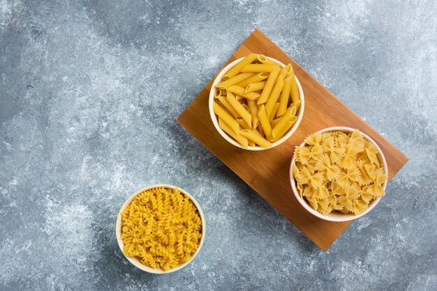 Different types of raw macaroni on wooden board.