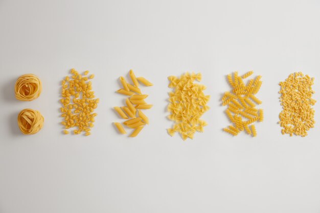 Different types of raw uncooked pasta on white background. Pasta nests, farfalle, tripolini, penne, fusilli can be used for sauces or dishes. Variety of Italian product. Various forms. Food concept