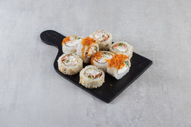 Different types of sushi rolls placed on a wooden board . 