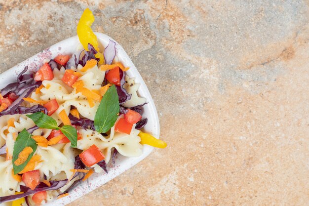 Different vegetables and farfalle pasta in a bowl on the marble surface