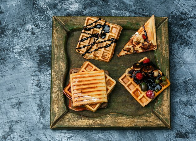 Different waffles on a bronze plate on a dark blue marble background. top view.