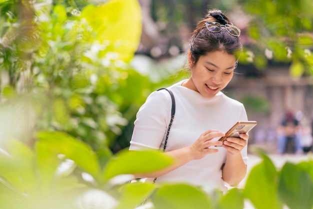 Цифровой кочевник, азиатская женщина, молодой взрослый, работающий в любом месте, общающийся, используя смартфон, контакт и встреча с новым образом жизни, веселым счастьем в кафе, парке, саду, концентрируется на работе